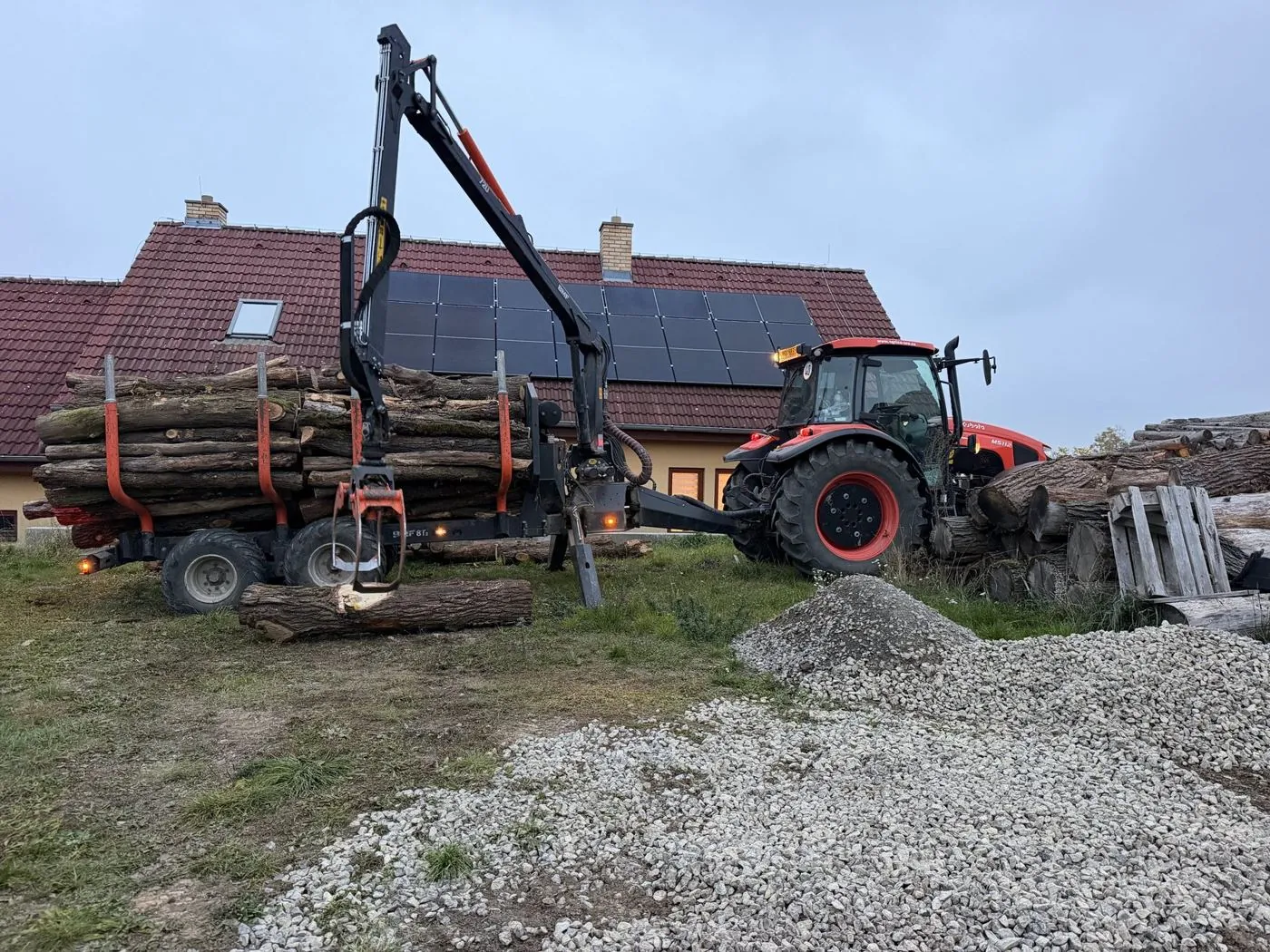 Traktor s naloženým vlekem z boku, ruka pokládá kládu na zem